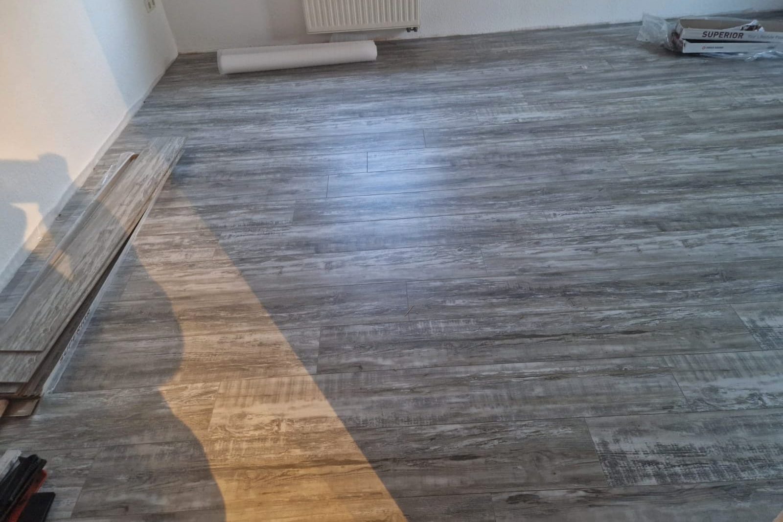 Frisch verlegter Klick-Vinylboden in Holzoptik, daneben restliche Dielen und Dämmunterlage