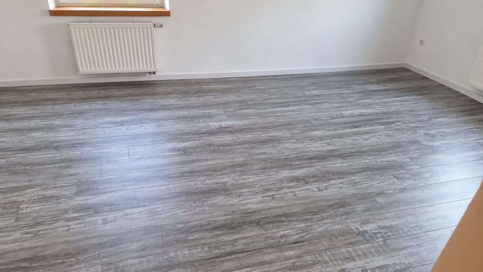 Nach der Arbeit: neu verlegter Klick-Vinylboden in Holzoptik mit weißen Sockelleisten ringsum